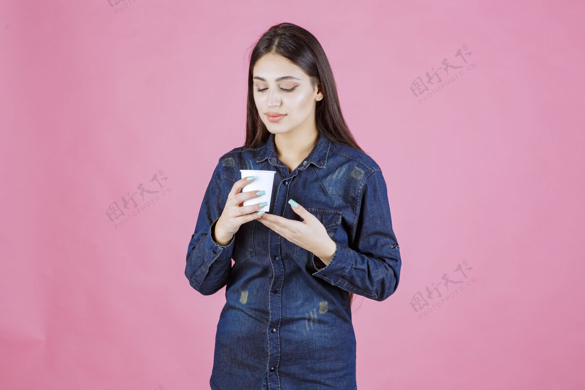 休闲穿着牛仔衬衫的女孩手里拿着一个咖啡杯 看上去若有所思 疑神疑鬼女人人冬天