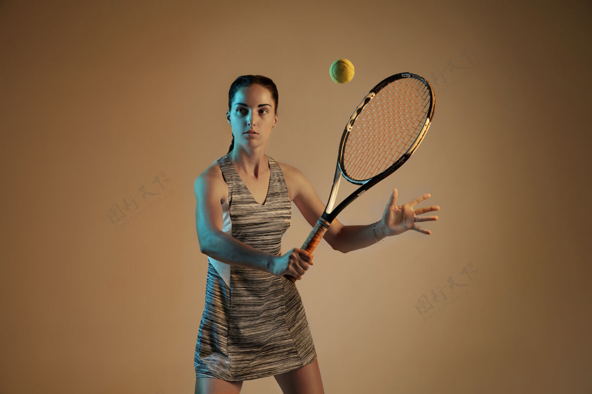 射击一位白人女子在混合霓虹灯下孤立地打网球 背景是棕色适合年轻女性运动员在运动比赛中运动或动作运动 运动 健康生活方式的概念明亮运动年轻人