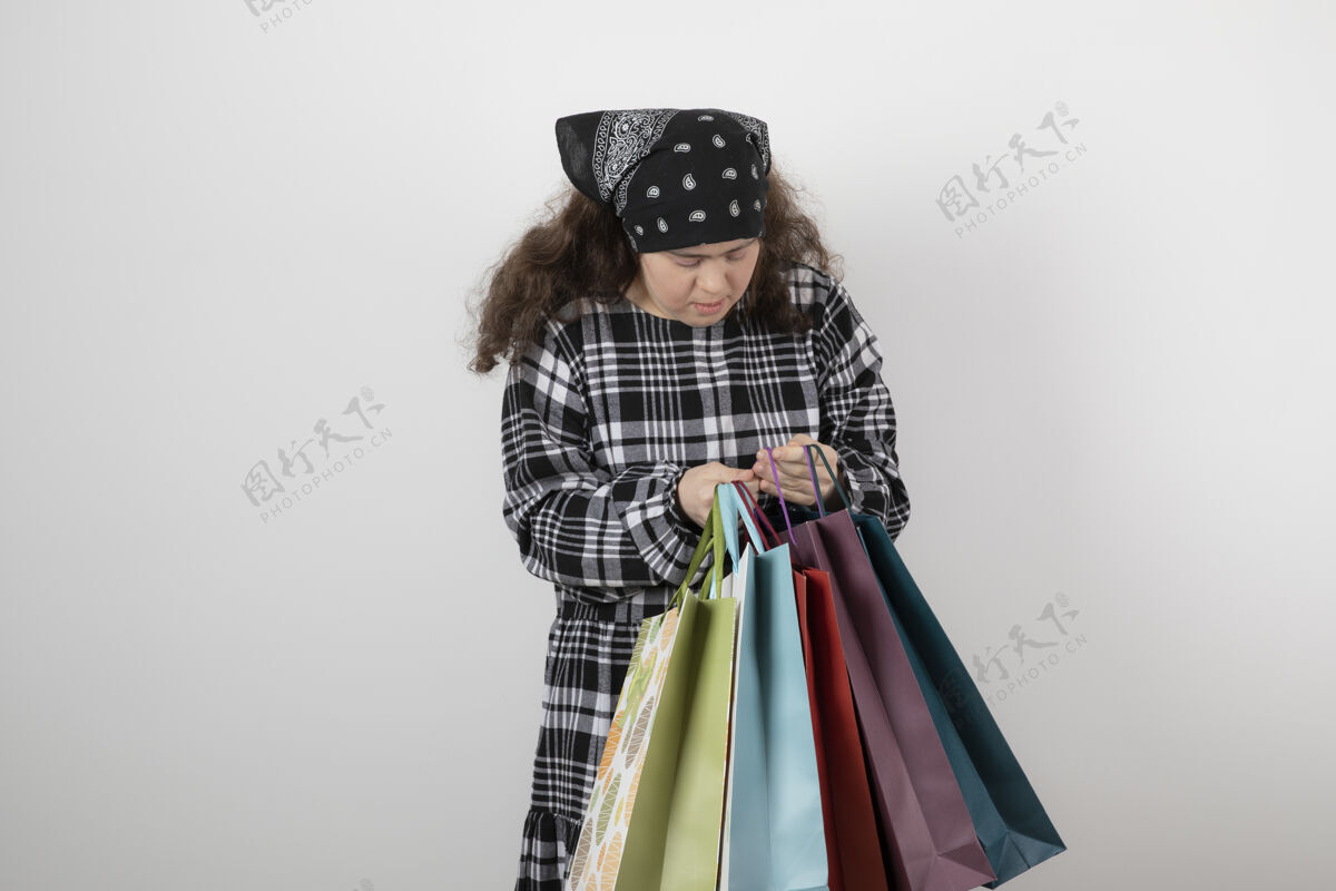 购物患有唐氏综合症的年轻女孩看着一堆购物袋的画像包挑战综合征