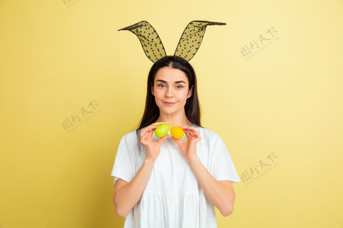 鸡蛋寻找彩蛋来了白人妇女作为一个复活节兔子在黄色的工作室背景复活节快乐的问候美丽的女模特人类情感的概念 面部表情 节日复制空间人类漫画兔子