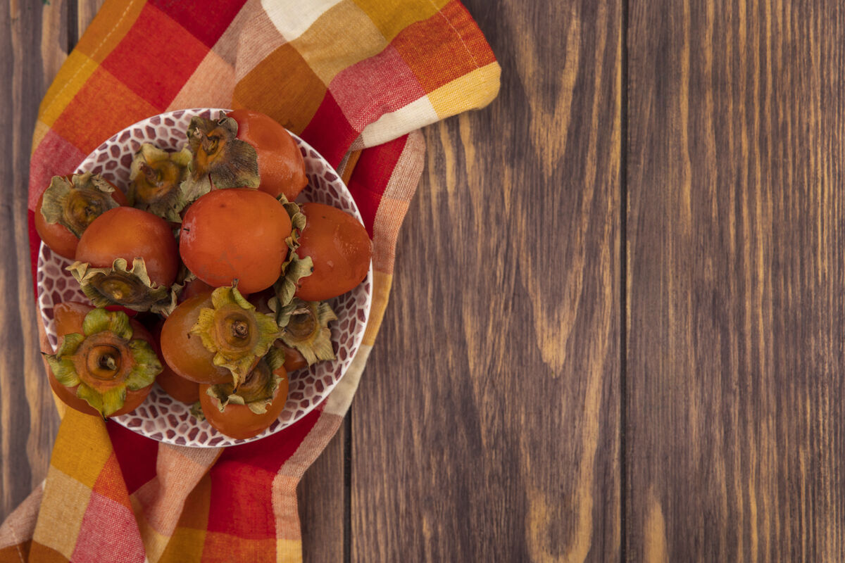 食物顶视图新鲜柔软多汁的柿子在一个碗上的格子布在木制背景与复制空间复制查看木头
