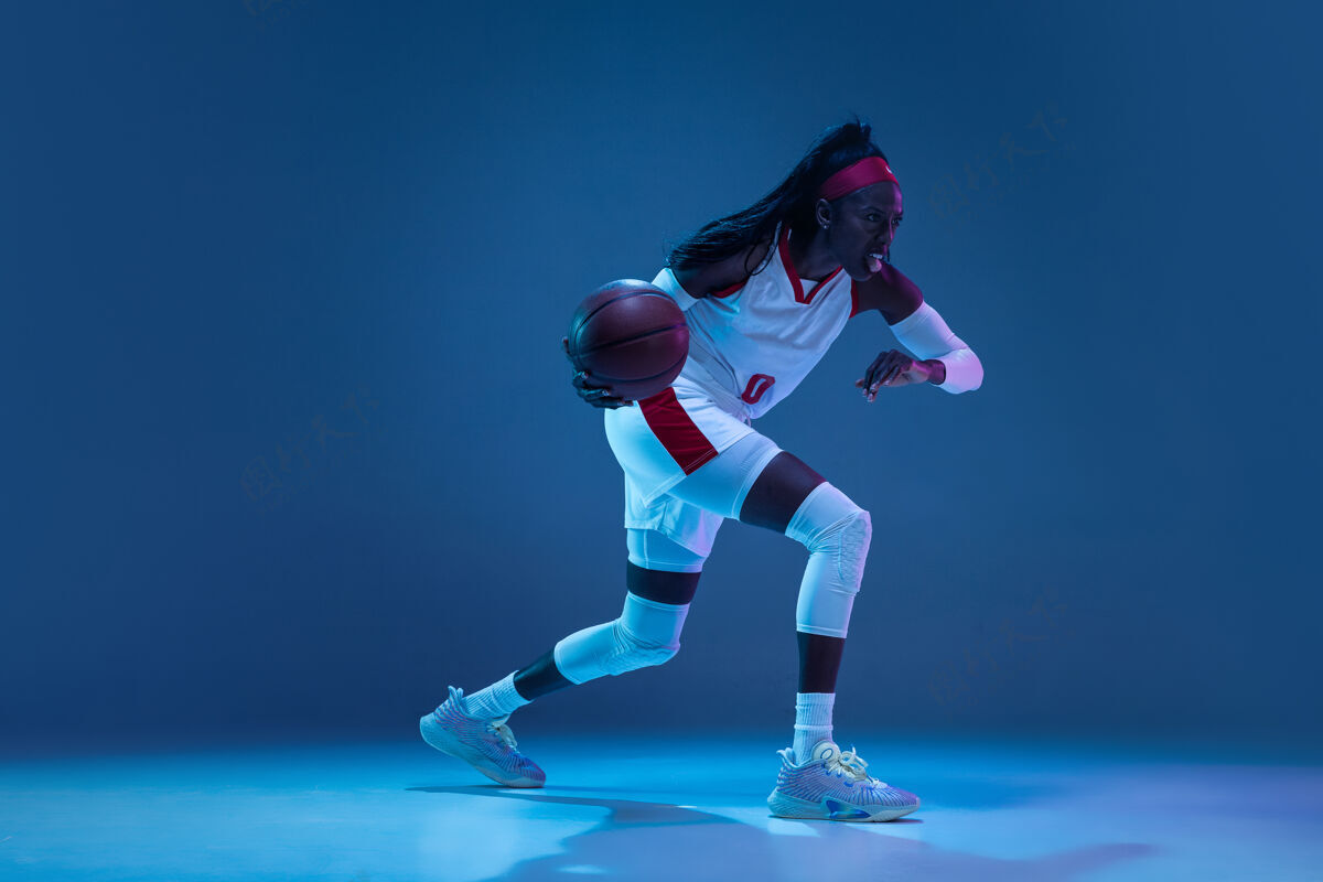 运动员美丽的非洲裔美国女篮球运动员在运动和行动中 在霓虹灯的蓝色墙壁上健康生活方式的概念职业体育爱好团队比赛赢家
