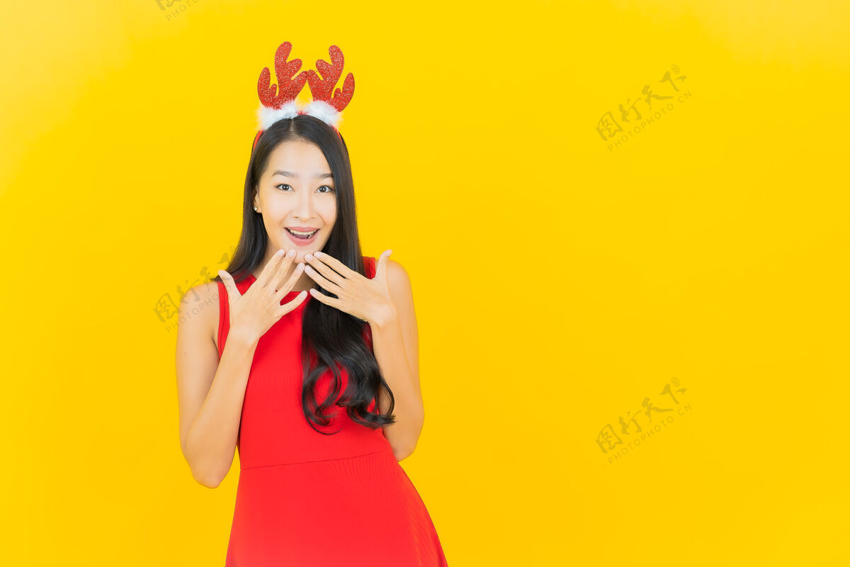 年轻肖像美丽的亚洲年轻女子戴圣诞帽或发带在黄色的墙上欢呼礼物快乐