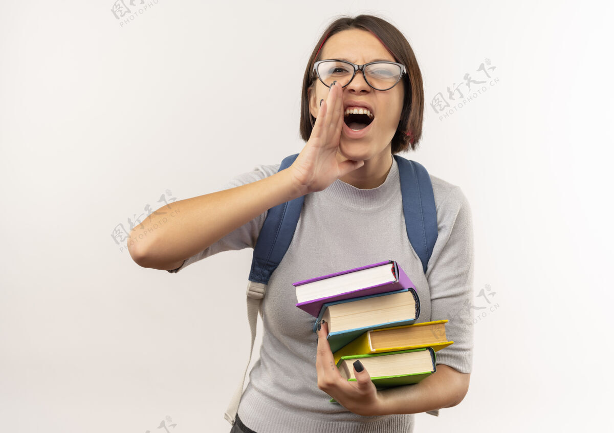 戴年轻的女学生戴着眼镜 背着书包 把手放在嘴边 对着一个被隔离在白色背景下的人喊叫抱年轻学生