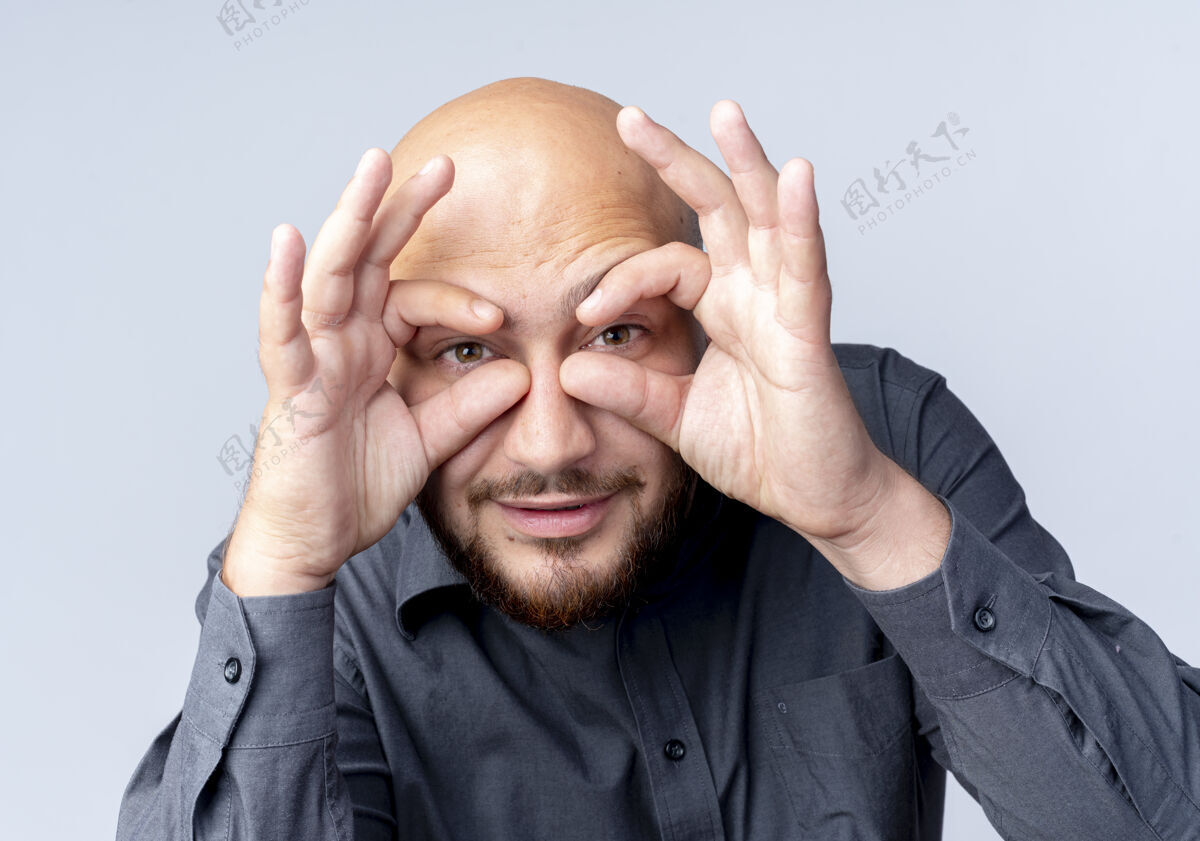 相机年轻的秃头呼叫中心的男人做着看镜头的手势 用双手作为望远镜 隔离在白色背景上望远镜呼叫手