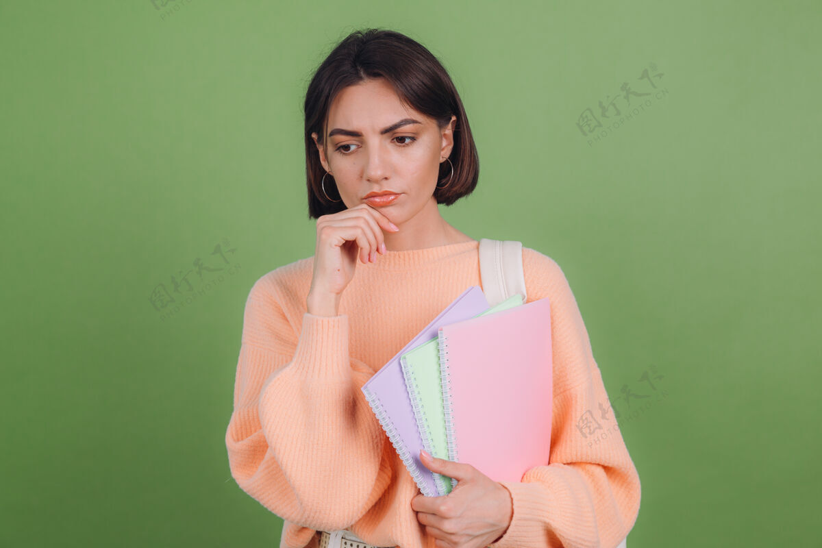 女人穿着休闲桃色毛衣的年轻女子被隔离在绿橄榄色的墙上学习任务文件
