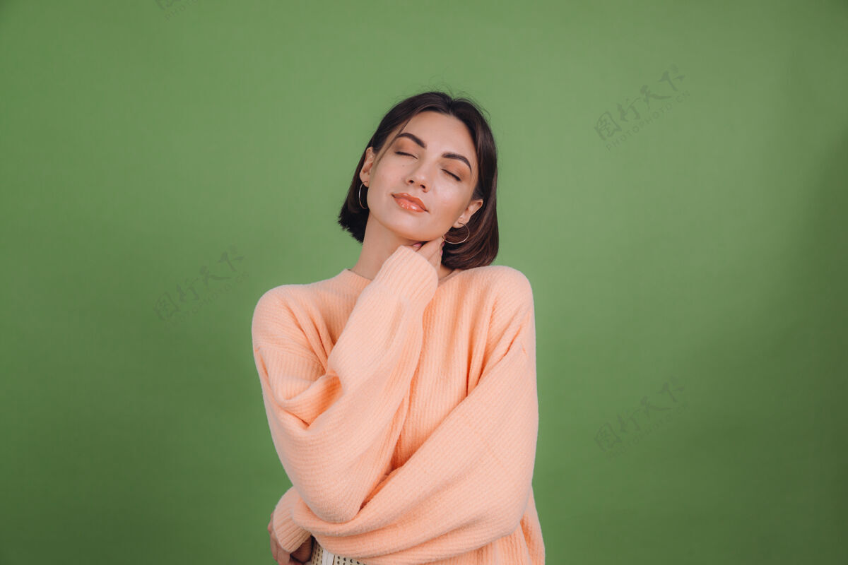 和平穿着休闲桃色毛衣的年轻女子被隔离在绿橄榄色的墙上调情眼睛嘴唇