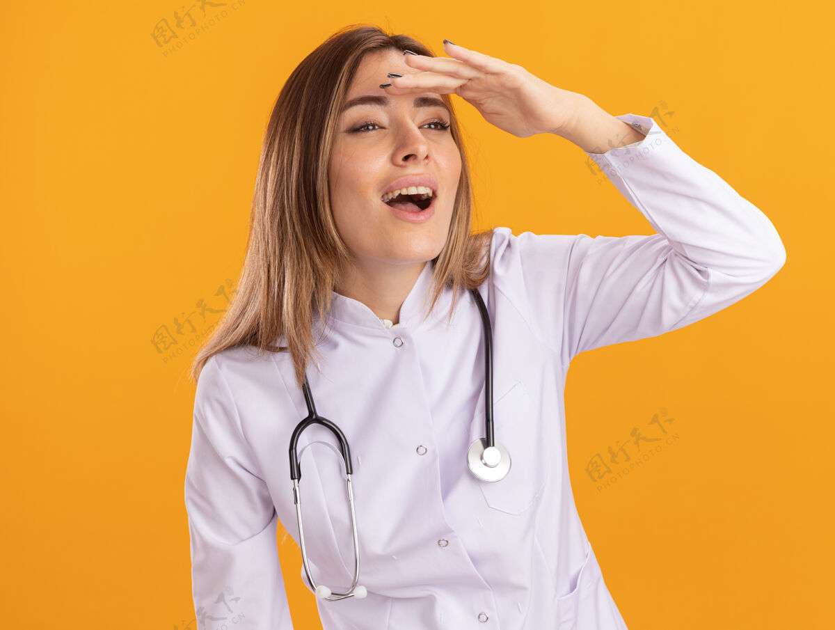 微笑微笑着看着身边年轻的女医生穿着医用长袍用听诊器看着远处隔离在黄色墙上的手穿女性医生