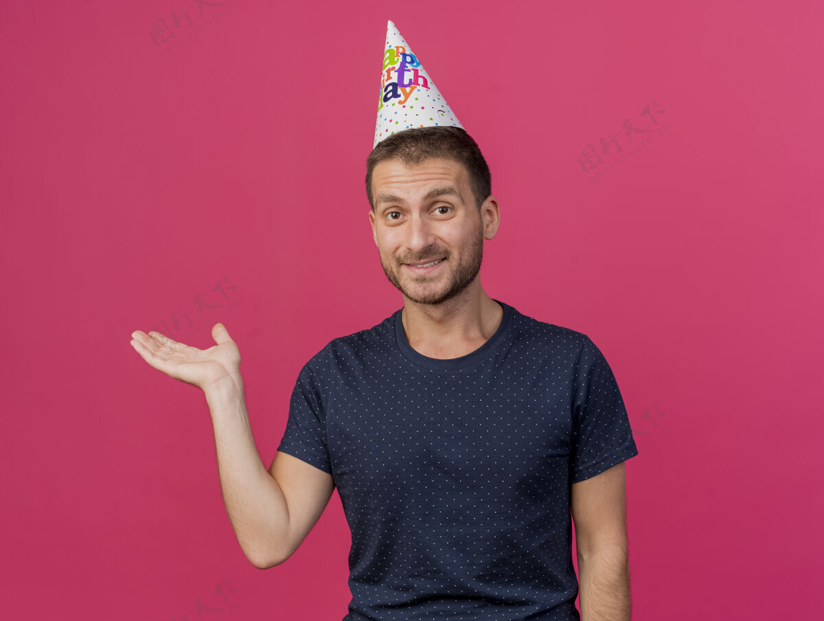 帽子戴着生日帽的白种人帅哥高兴地把手张开 孤立地放在粉色背景上 留有复制空间生日打开粉色