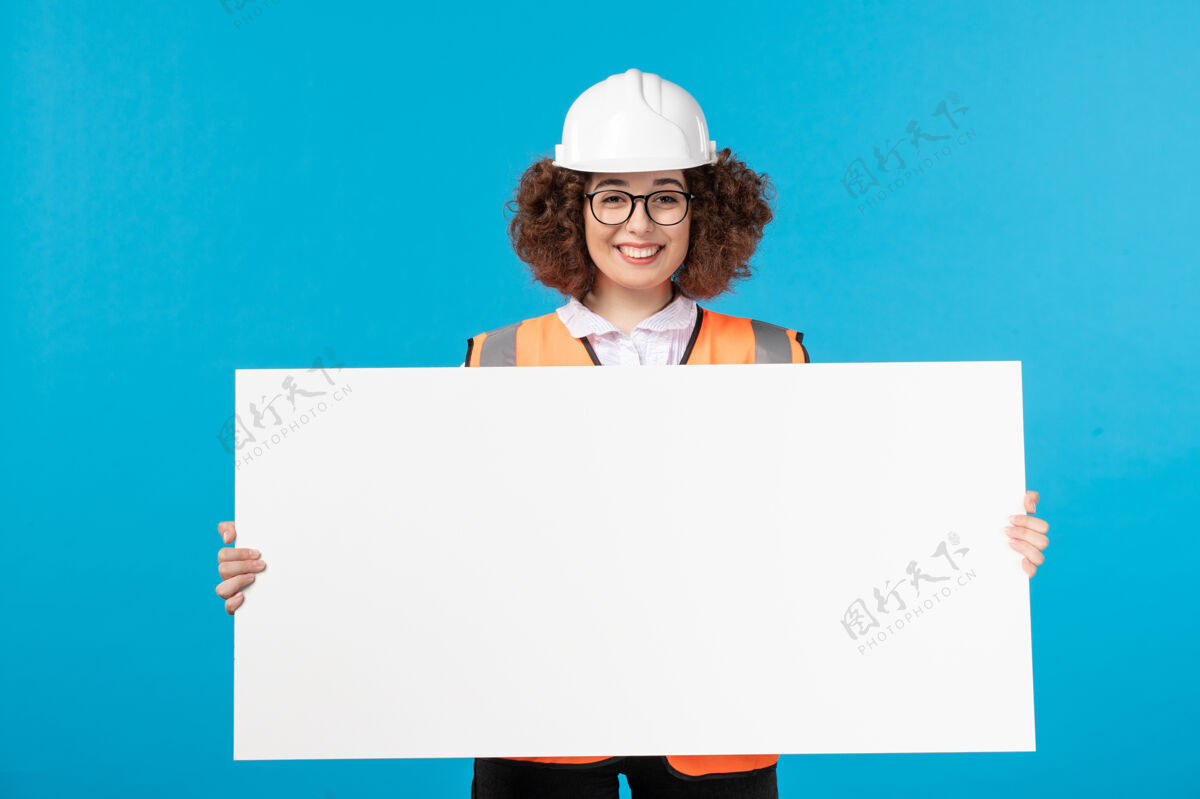工人身着制服的女建筑工人正拿着蓝色墙壁上的白色普通办公桌蓝色人制服