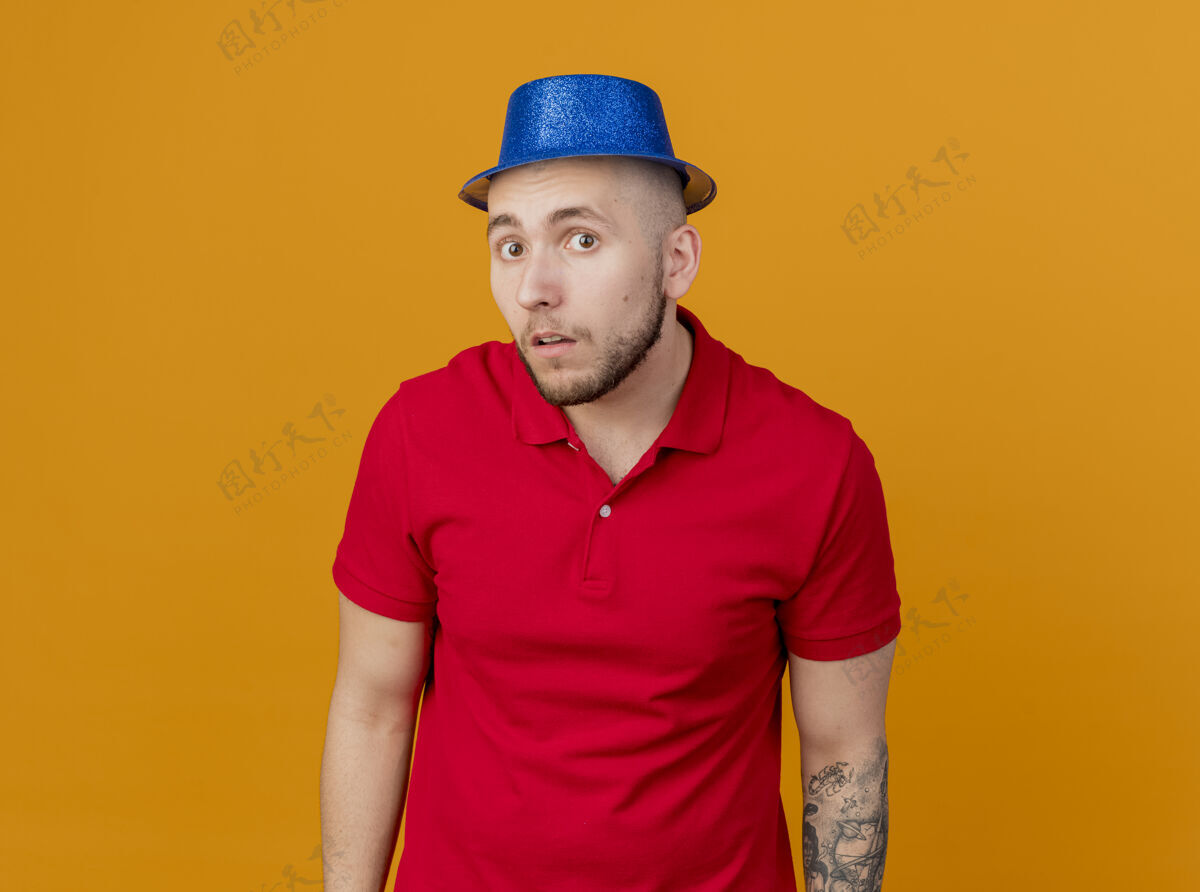 太空令人印象深刻的年轻英俊的斯拉夫党的家伙戴着党的帽子 看着相机孤立的橙色背景与复制空间斯拉夫人年轻人帽子
