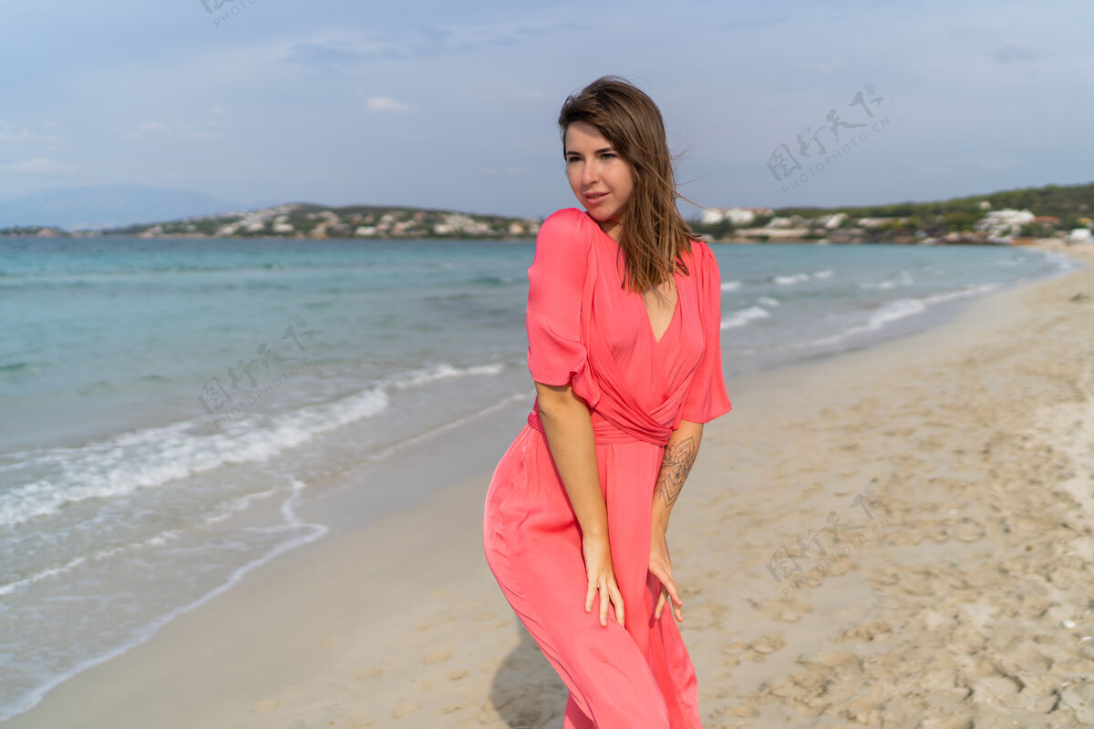 海洋性感的黑发女人手上拿着塔图 穿着粉色连衣裙在海滩上摆姿势活跃女人身体