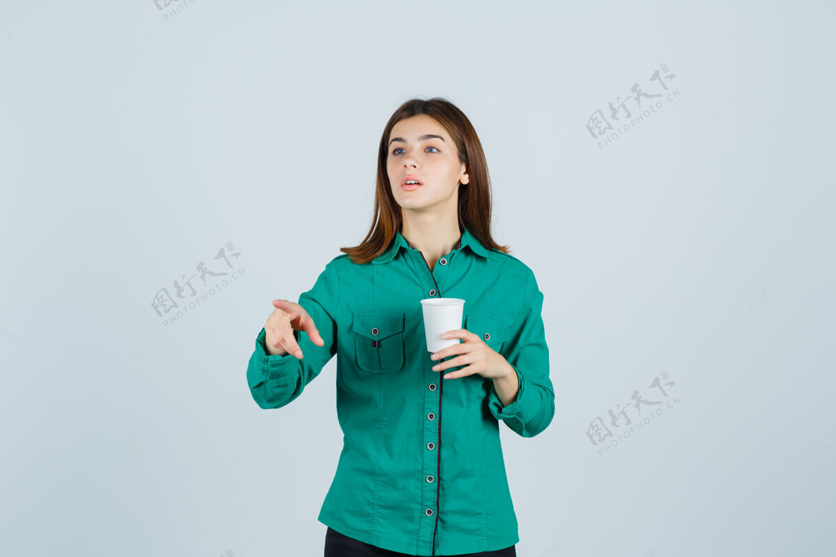 人穿着衬衫的年轻女士手里拿着一杯塑料咖啡 指着别处 专注地看着前方时尚女人指向