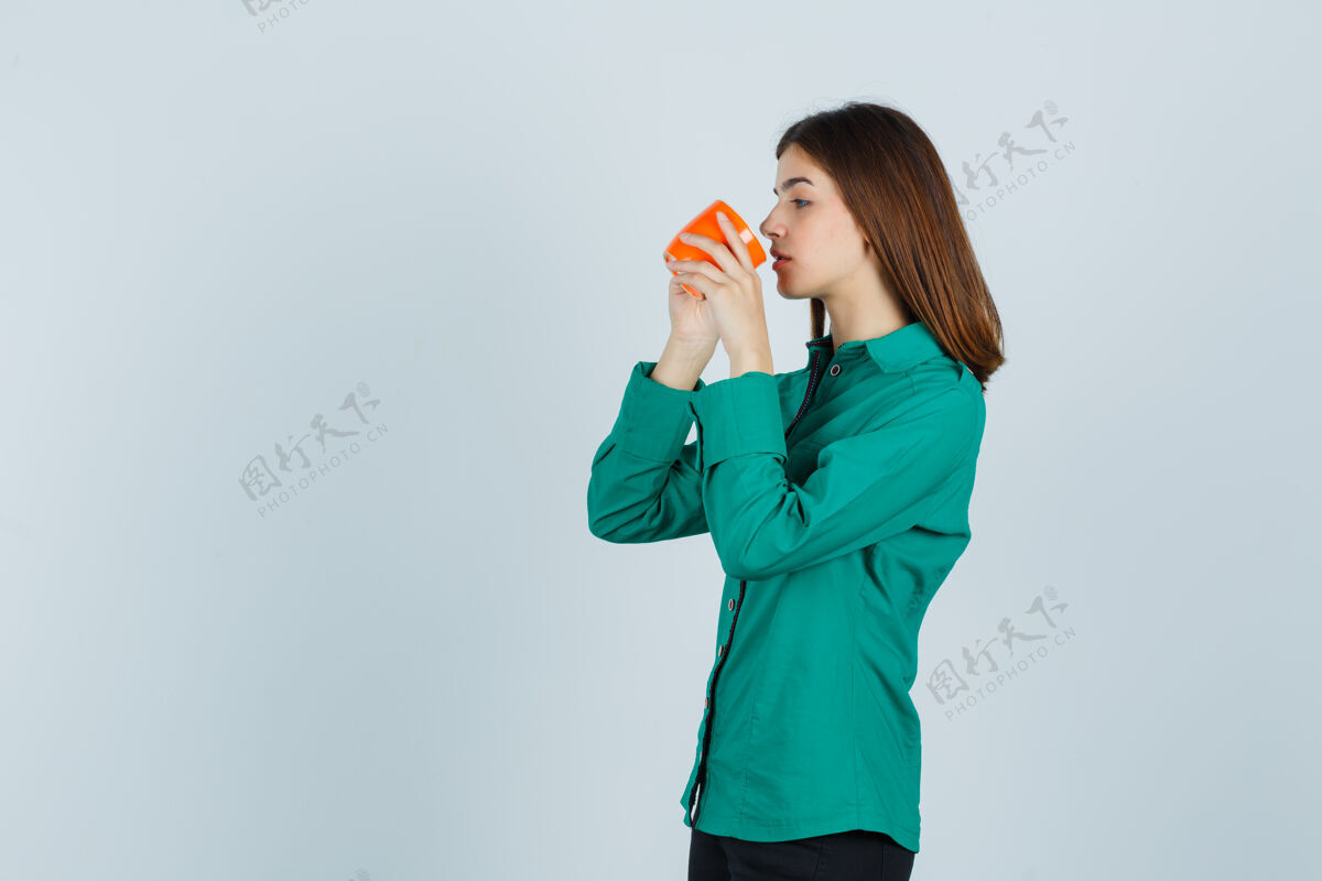 肖像年轻的女士穿着衬衫从橘色杯子里喝茶 看起来很专注正视图专注牙齿年轻