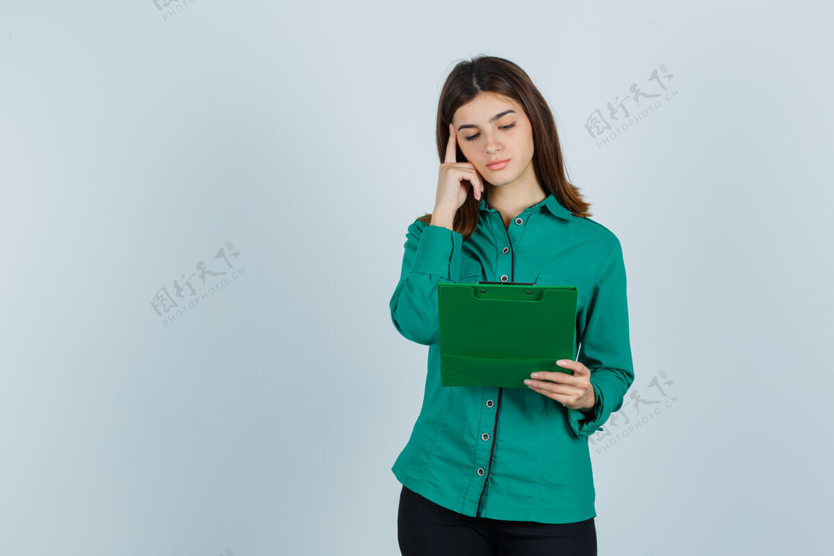 衬衫穿着绿色上衣 黑色裤子的年轻女孩看着剪贴板 把食指放在太阳穴上 神情沉思 俯瞰前方模特裤子人