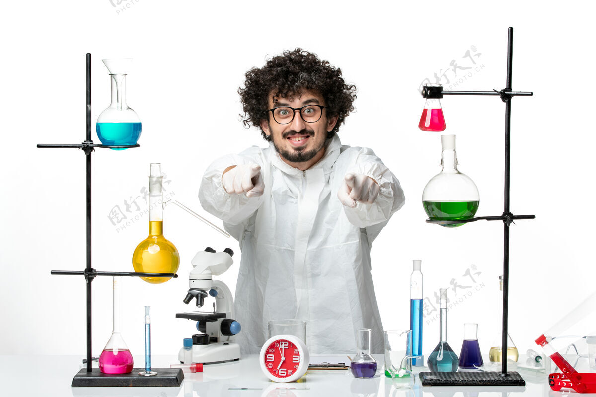 实验室外套正面图身着特殊套装的年轻男性科学家站在桌子旁 白色桌子上摆着解决方案视图站着周围