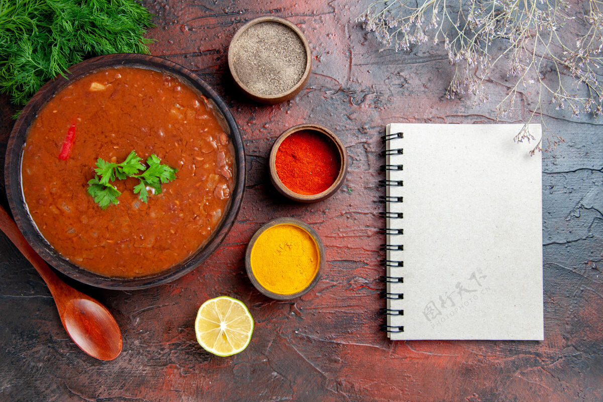 盘子经典的番茄汤放在一个棕色的碗里 不同的香料和笔记本放在五颜六色的桌子上晚餐碗午餐
