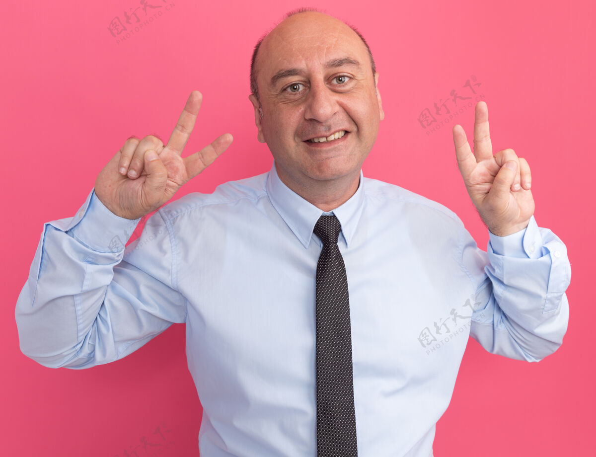 穿微笑的中年男子身穿白色t恤 打着领带 在粉红色的墙上显示出和平的姿态男人秀手势