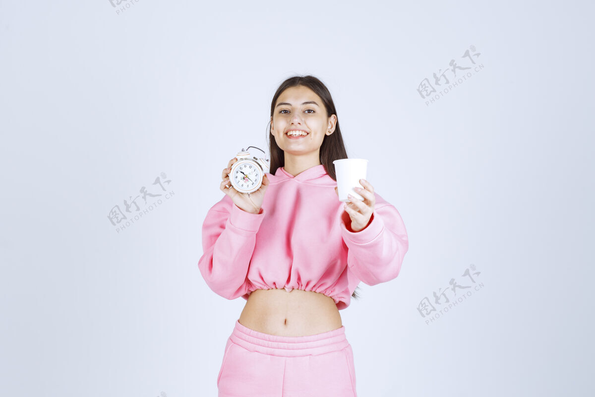 微笑穿着粉色睡衣的女孩手里拿着闹钟和一杯咖啡积极促销人体模特
