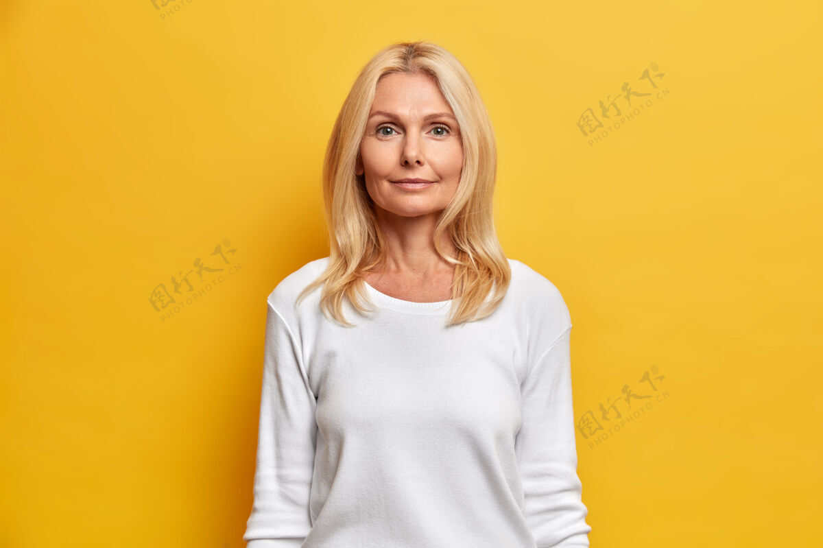 自信照片中的中年女性容貌姣好 满脸皱纹 自然美丽 金发直视镜头 表情平静 身着白色休闲套头衫老年人外表奶奶