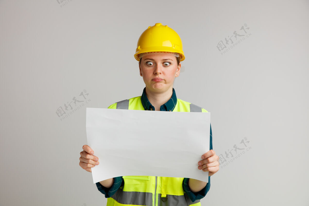 白色笨手笨脚的年轻女建筑工人 戴着安全帽 穿着安全背心 撅着嘴看着纸嘴唇头盔年轻