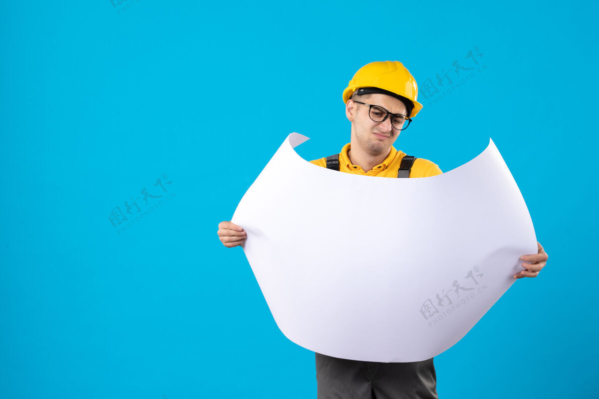 工作身穿黄色制服的男建筑工人的正视图 蓝色平面图施工工程师制服