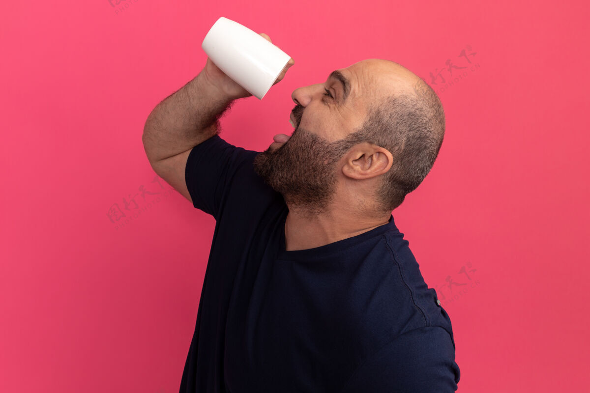 胡子穿着海军蓝t恤的快乐大胡子男人站在粉红色的墙上 手里拿着一杯茶要喝伙计茶架子