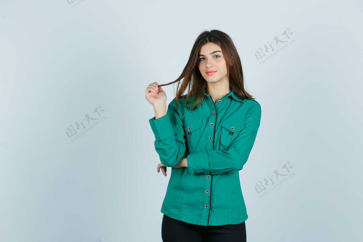 女士年轻的女性拿着她的栗色头发和手指在绿色衬衫 看起来很高兴 前视图头发女孩休闲