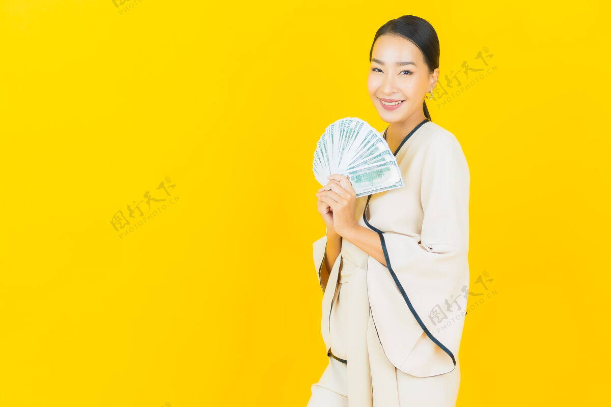 商业妇女黄墙上有一幅美丽的年轻亚洲商人的画像 她手里拿着很多现金和小猪存钱罐退休利润赚取