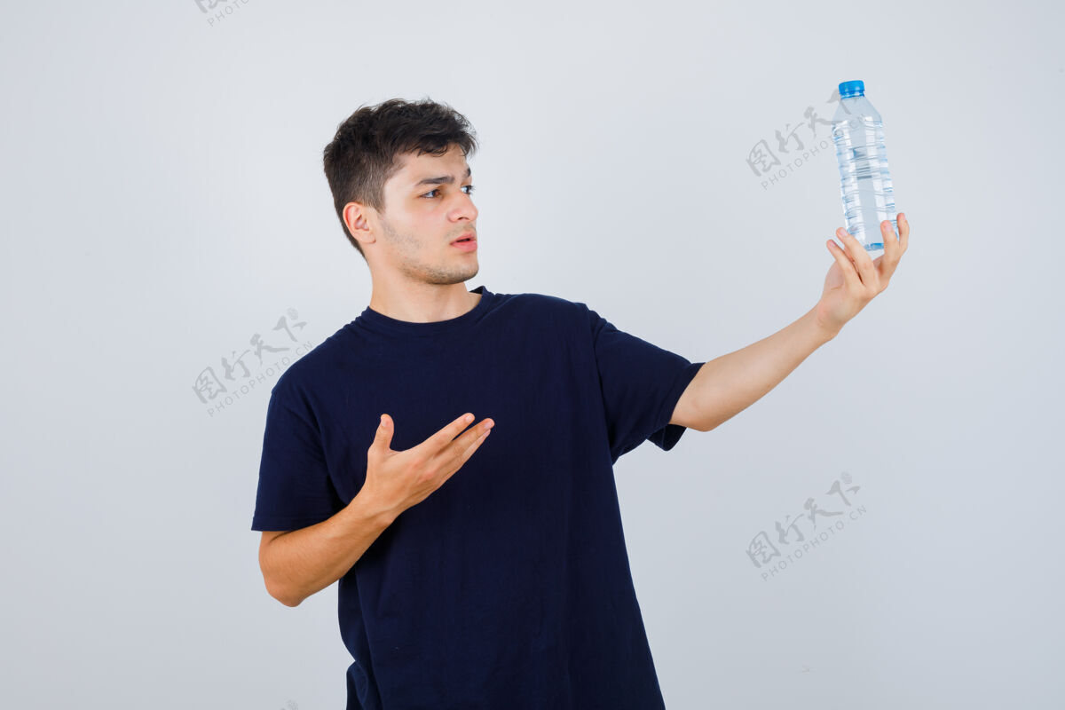 年轻一个年轻人展示着一瓶水 穿着黑色t恤 看上去很困惑正视图问题决定胡子