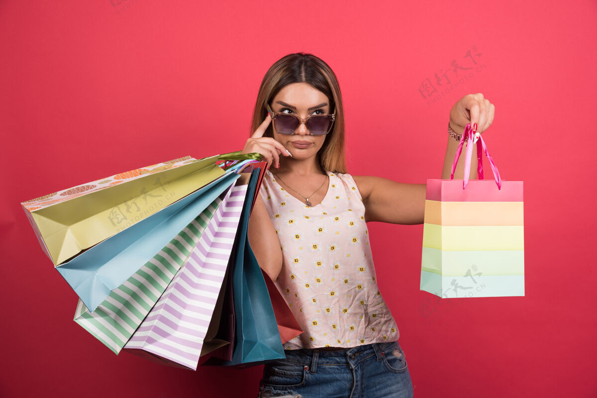 购买戴眼镜的女人把她的购物袋放在红墙上购物包咖啡