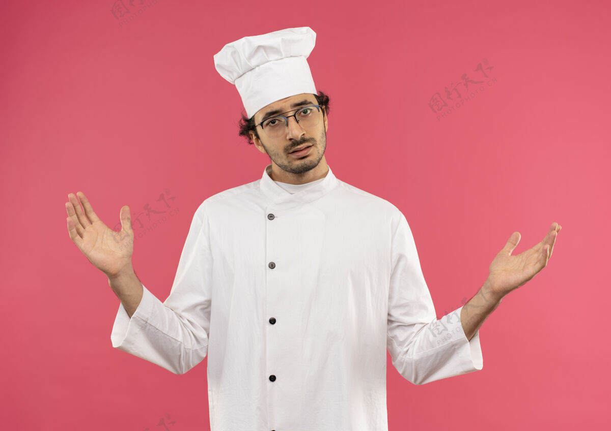 年轻困惑的年轻男厨师穿着厨师制服和眼镜摊开双手手男人厨师