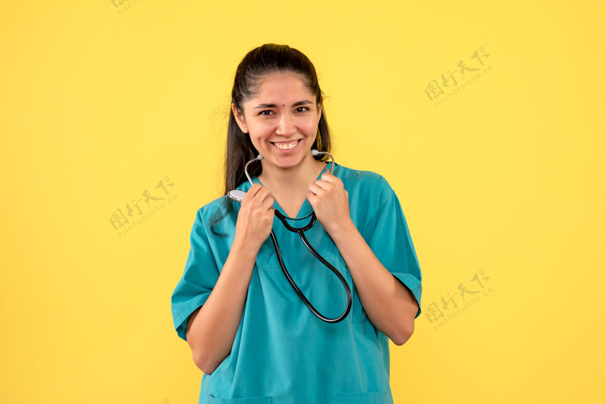 制服正面图笑女医生手持听诊器站在黄色背景上站听诊器背景