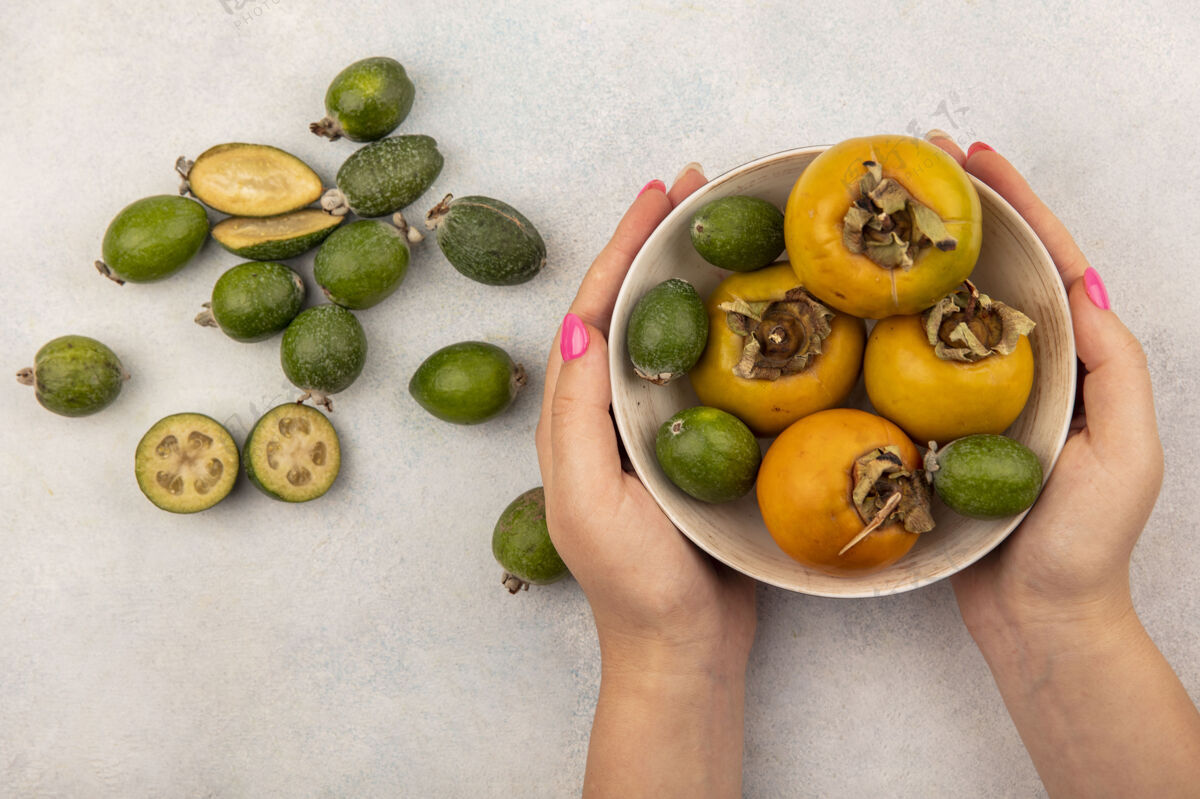 食物俯视图中的女性手拿着一碗绿色的熟柿子 柿子放在灰色的表面上健康肥肉碗