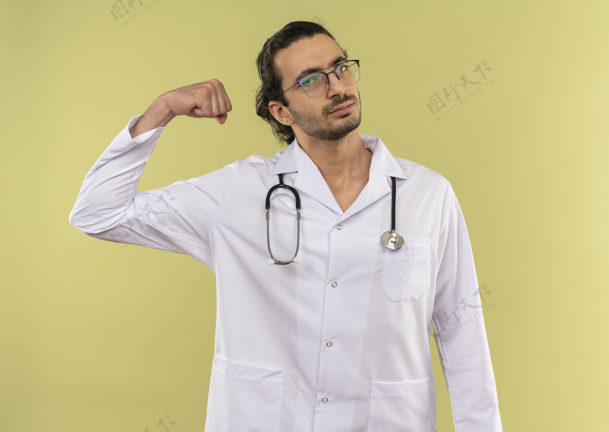 光学自信的年轻男医生戴着眼镜穿着白袍用听诊器做着有力的手势强壮手势长袍