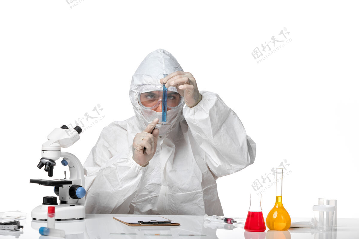 西装正面图：男医生穿着防护服 戴着面罩 因为covid拿着装有蓝色溶液的烧瓶 浅白色空间化学医生前