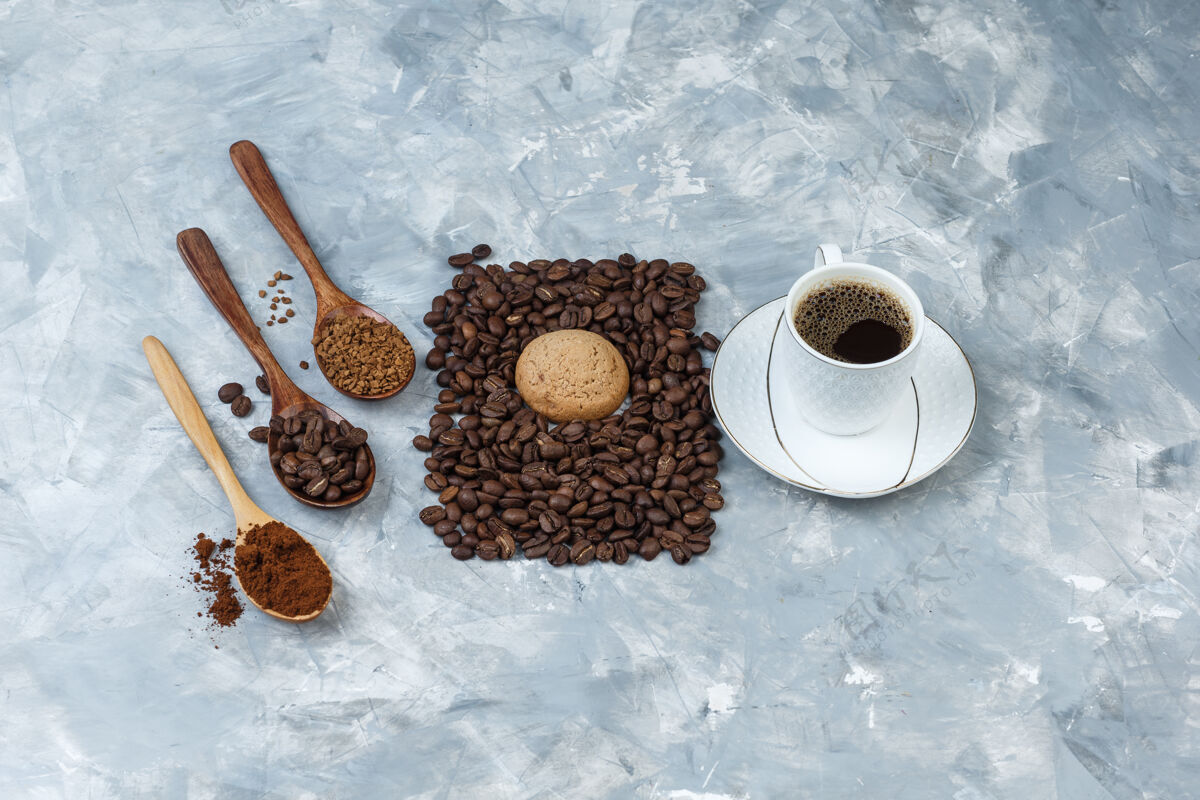 豆子平铺饼干 一杯咖啡加咖啡豆 速溶咖啡 咖啡粉放在浅蓝色大理石背景上的木勺里水平热水平香味