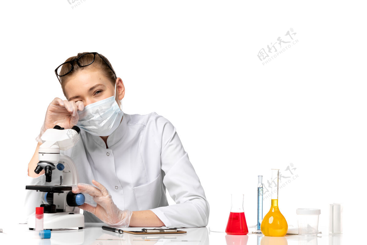 病毒前视图：女医生穿着医疗服 戴着面罩 在浅白色空间使用显微镜疾病套装显微镜