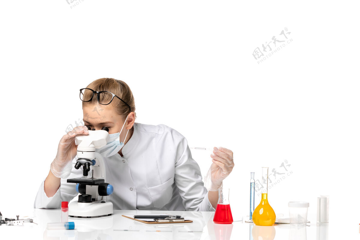 秘书前视图：女医生穿着医疗服 戴着口罩 由于戴着隐形眼镜 在白色空间上使用显微镜穿戴大流行病毒