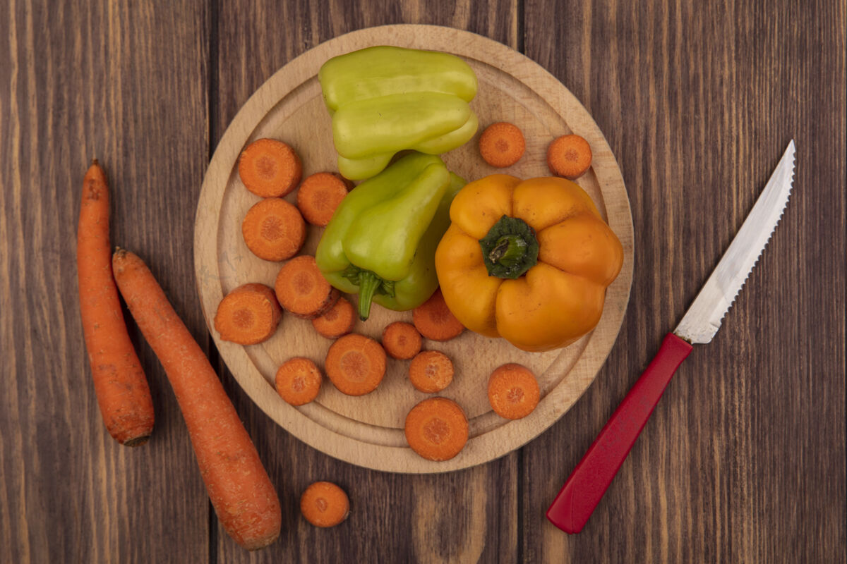 营养顶视图五颜六色的甜椒在一个木制的厨房板与切碎的胡萝卜与胡萝卜刀隔离在一个木制的表面蔬菜胡椒自然