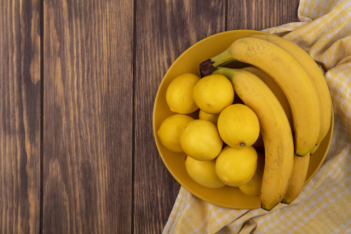 食物黄色格子布上黄色盘子上的黄皮柠檬俯视图 木制表面上有香蕉和复印空间衣服新鲜配料
