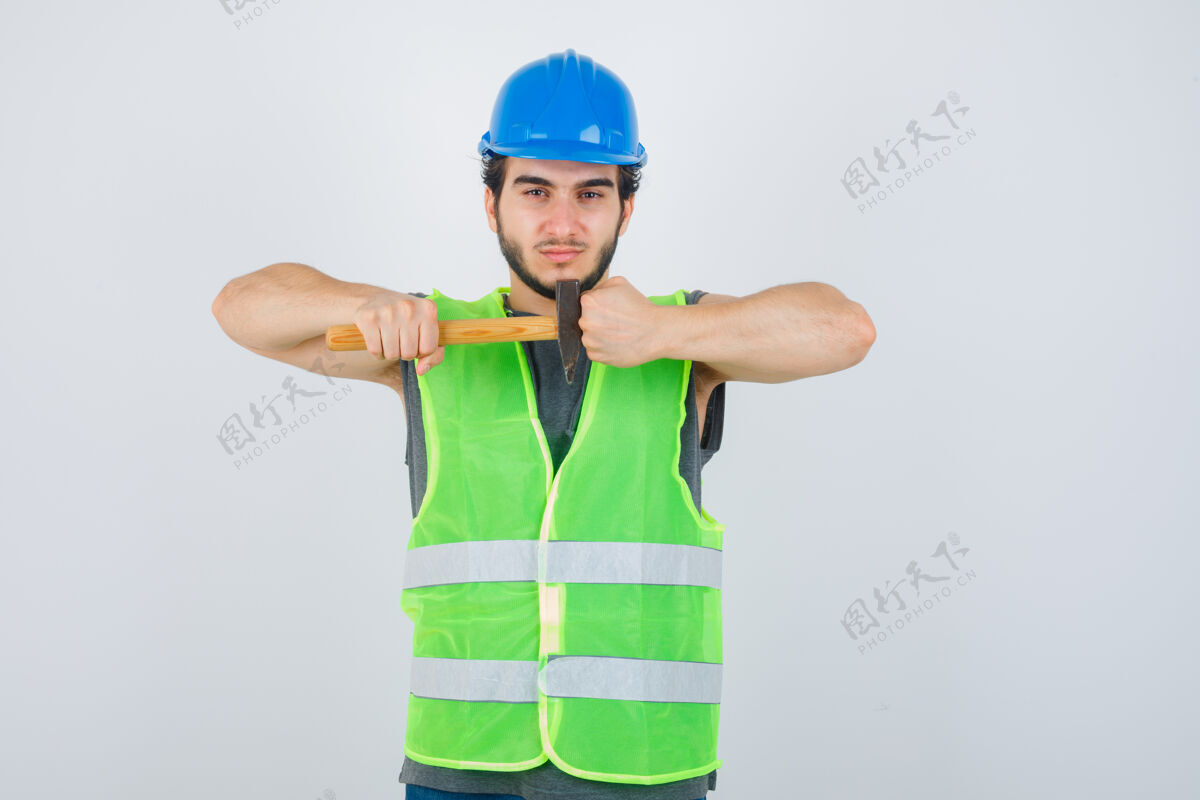 人年轻的建筑工人手持锤子 穿着工作服 握紧拳头 看上去很自信正视图英俊工作服酷