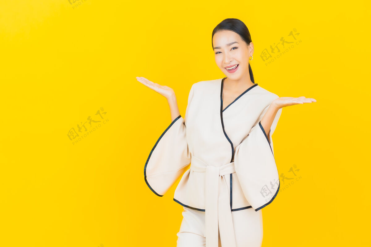 时尚美丽的亚洲年轻商业女性在黄色墙上穿着白色西装微笑的画像手臂人行政