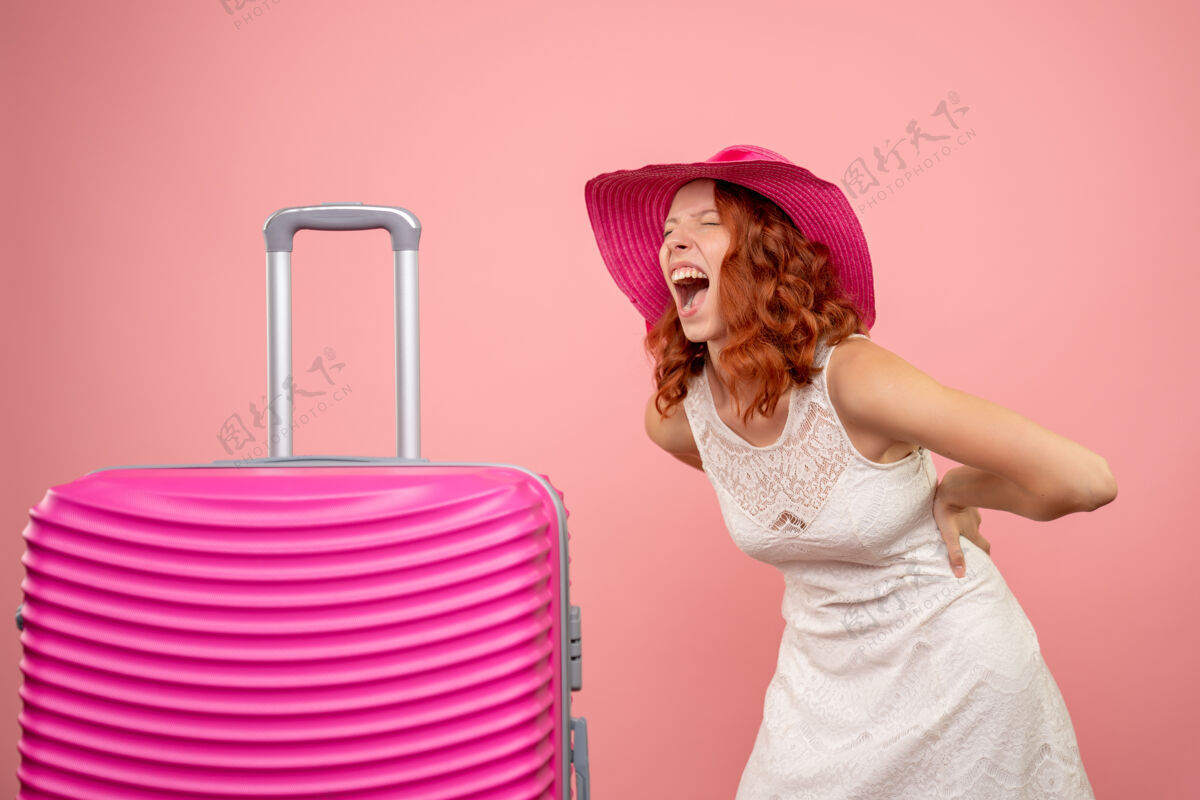 购物年轻的女性游客与粉红色的帽子和粉红色的墙壁上的包的正面视图人夏天航行