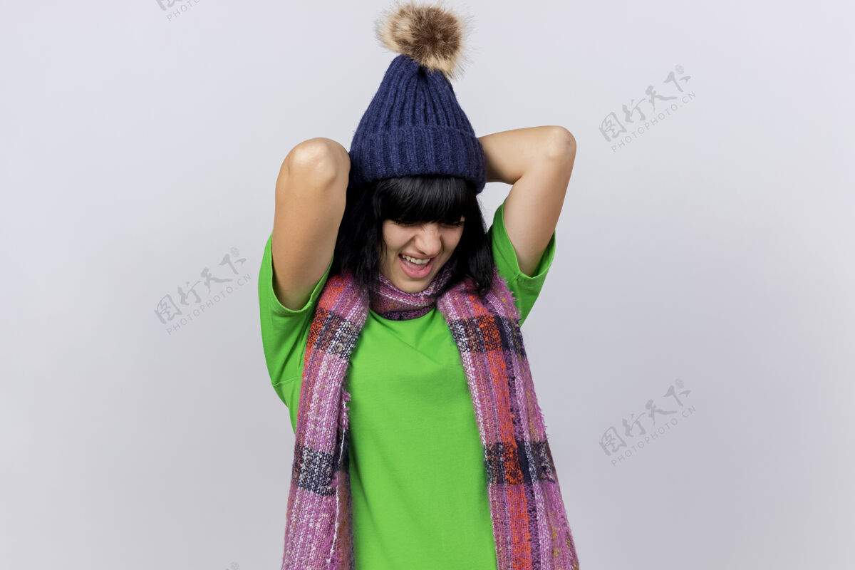 围巾疼痛的年轻白种女孩戴着冬天的帽子 戴着围巾 双手放在背后 闭着眼睛 隔离在白色的墙壁上 留着复制空间疾病帽子保持