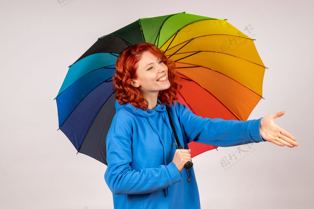 五颜六色白色墙壁上带着彩色雨伞的年轻女性的正视图彩虹掩护伞