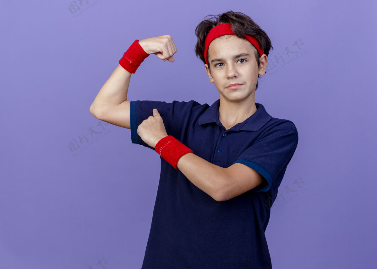 腕带自信的年轻帅气的运动男孩戴着头带和带牙套的腕带做着强烈的手势 指着他隔离在紫色墙壁上的肌肉复制空间帅气头带运动