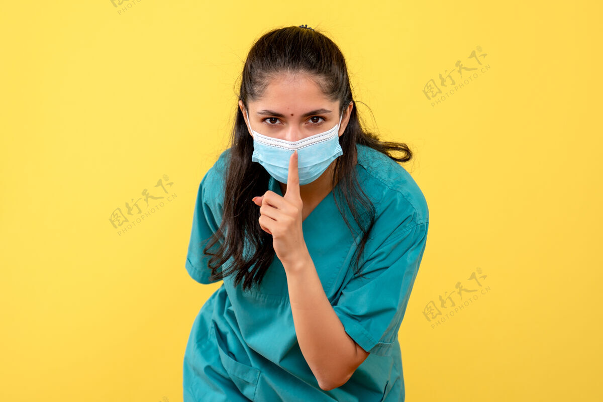 约束黄色墙上戴着医用口罩的漂亮女医生在做嘘标志肖像脸人