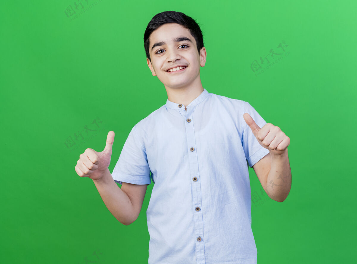 表演微笑的年轻白人男孩在绿色的墙上竖起大拇指表达拇指男孩