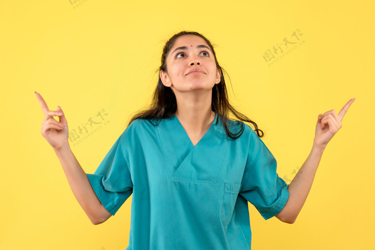 成人美丽的女医生站在黄色的墙上仰望前方护士医学微笑